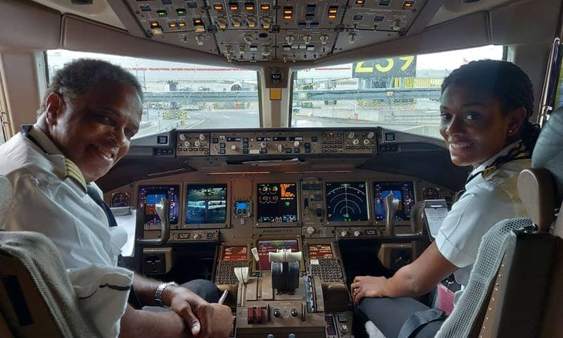 Zoey and her dad seated on the flight deck, turn and smile at the camera.